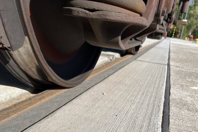 Detailbild, das die Oberflächenstruktur einer Gleistragplatte zeigt. Die Gleistragplatte ist im öffentlichen Bereich eingebaut und wird in dem Moment der Aufnahme gerade von einem Zug befahren.