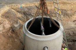 Montage eines Havarieschachts auf einer Baustelle. Der Schacht wird mit Ketten in eine Baugrube gesetzt.