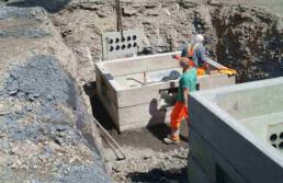 Das Bild zeigt die Montagearbeiten eines Aufbauschachts. Zwei Bauarbeiter installieren den Schacht in einer ausgehobenen Grube.